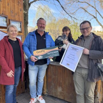 Die Geschäftsführung des GeoFly GmbH übergibt an den Zoodirektor David Pruß, Ph.D. einen Gutschein 10 Schulklassenführungen und bekommt die Pinguin-Patenurkunde vom Zoochef überreicht. Im Hintergrund Pinguin Pit mit Tierpflegerin.