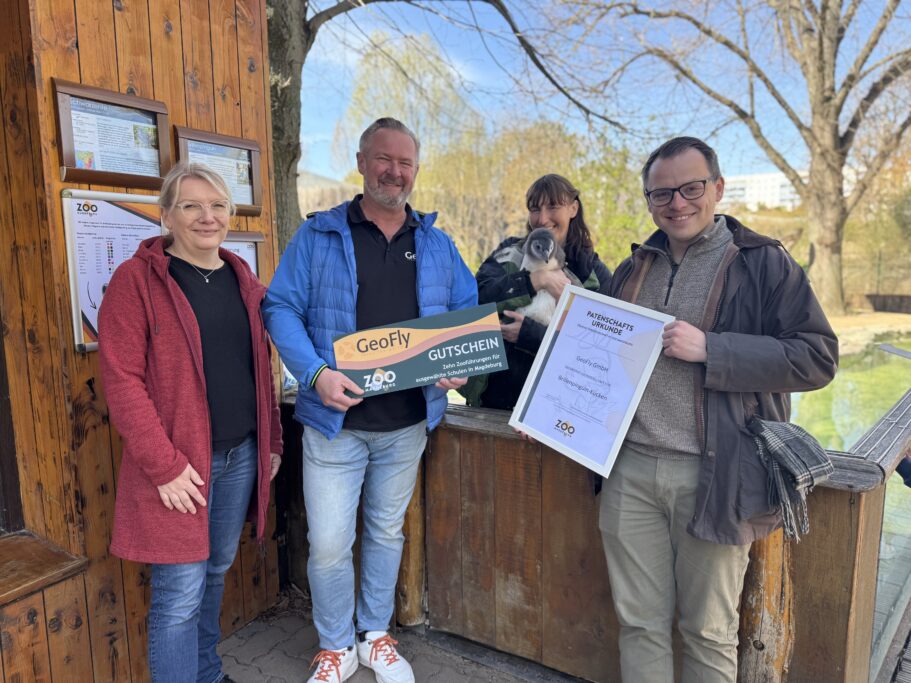Die Geschäftsführung des GeoFly GmbH übergibt an den Zoodirektor David Pruß, Ph.D. einen Gutschein 10 Schulklassenführungen und bekommt die Pinguin-Patenurkunde vom Zoochef überreicht. Im Hintergrund Pinguin Pit mit Tierpflegerin.